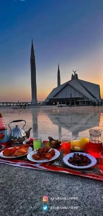 Sunset view of mosque with reflective surface and spread of food in foreground.