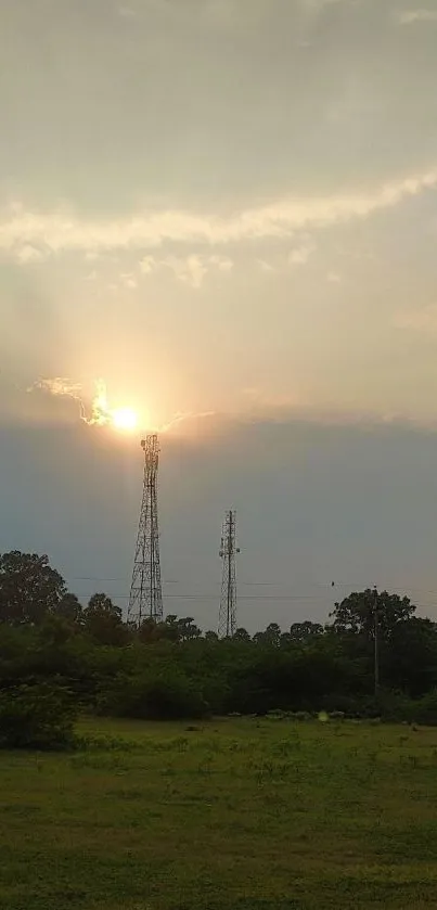 Beautiful sunset over green fields with silhouetted trees and towers.