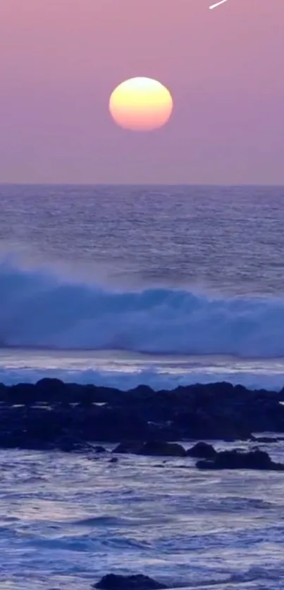 Purple sunset over ocean waves with rocky shore in view.