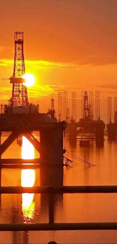 Sunset over oil rigs with orange sky reflection.