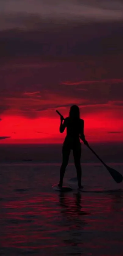 Silhouette of a paddleboarder against a crimson sunset over tranquil waters.