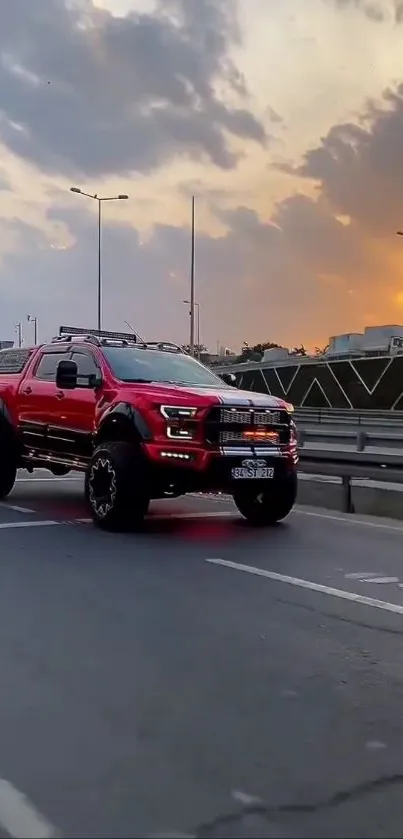 Red truck driving on a city highway at sunset with dramatic sky.