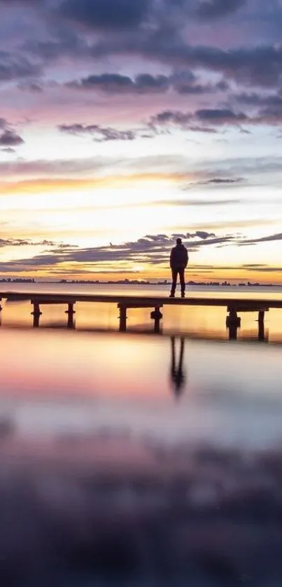 Silhouette on a dock with sunset reflection over water and vibrant evening sky.