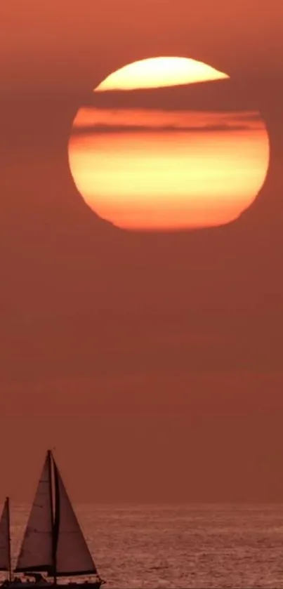 A sailboat glides across the ocean under a fiery sunset sky.