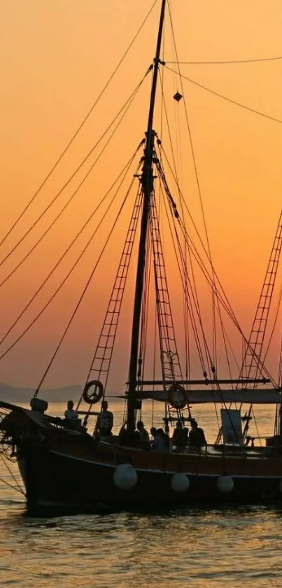 Sailing ship silhouette against an orange sunset over the ocean.