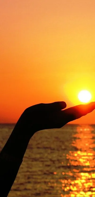 Silhouette of a hand catching a sunset over the ocean.