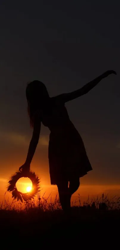 Woman's silhouette at sunset holding a wreath in artistic pose.
