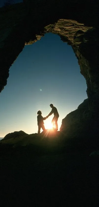 Silhouetted couple under rock arch at sunset by the sea.