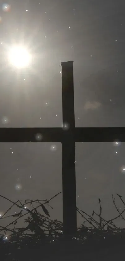 Silhouette of cross with sun shining in background on a dark sky.