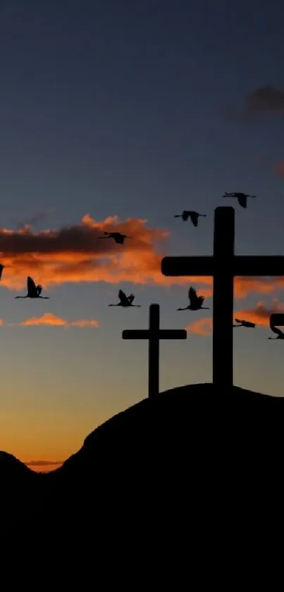 Silhouetted crosses at sunset with birds flying and scenic mountains.