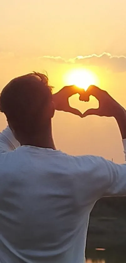 Silhouette making heart gesture against an orange sunset.