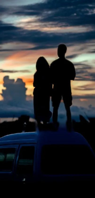 Silhouetted couple on van roof at sunset.