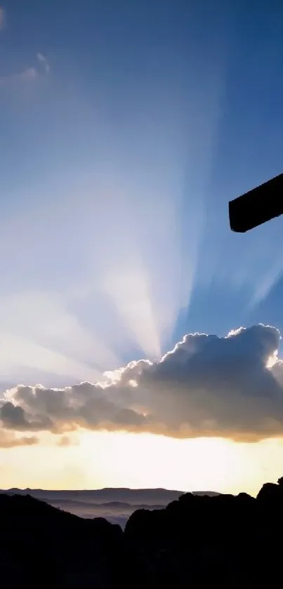 Silhouetted cross against sunset sky with mountains.