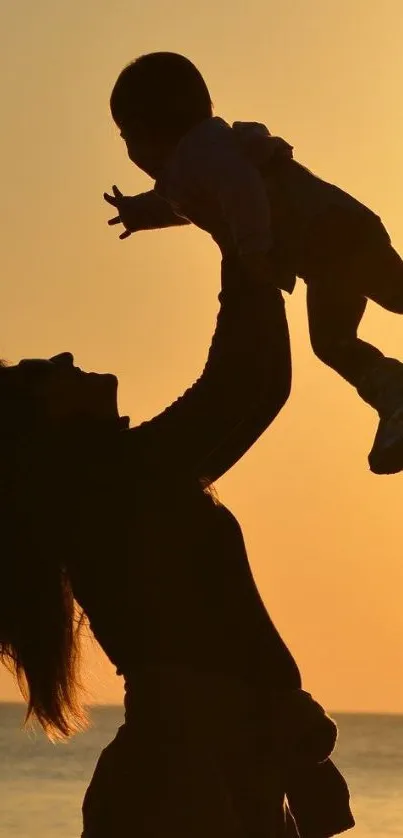 Silhouette of a mother lifting her child during a stunning seaside sunset.