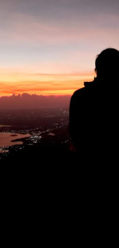 Silhouette against a vibrant orange sunset over the cityscape.