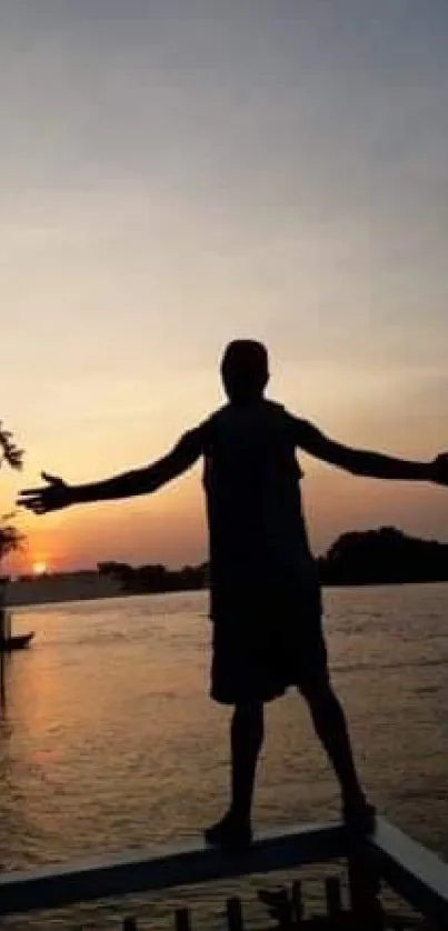 Silhouette of a person at sunset by the water, arms outstretched.