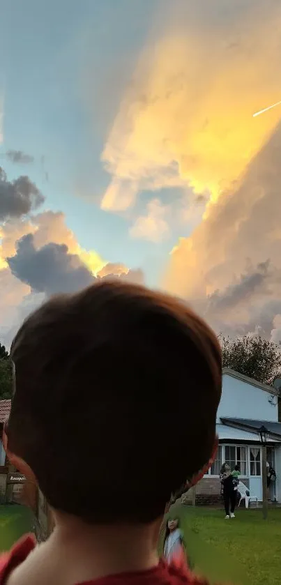 Boy looking at sunset sky with clouds and a house.