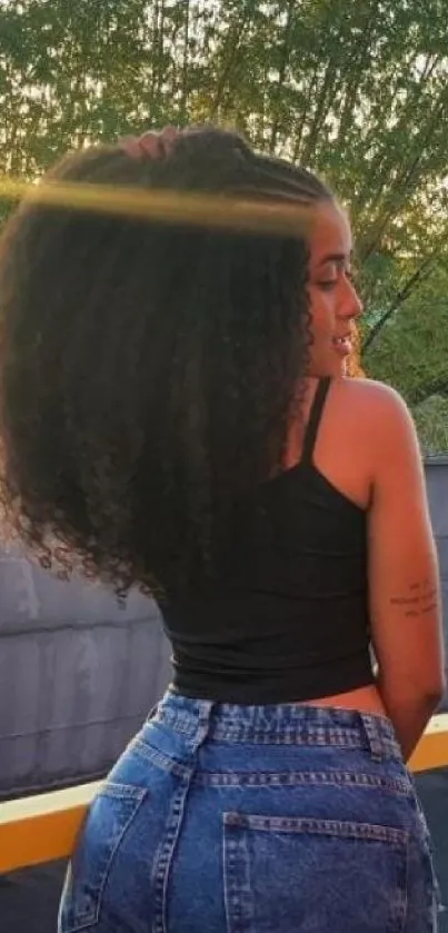 Woman in denim at sunset in urban setting, curly hair flowing.