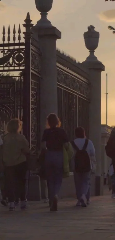 People walking near an ornate gate at sunset, creating a warm urban scene.