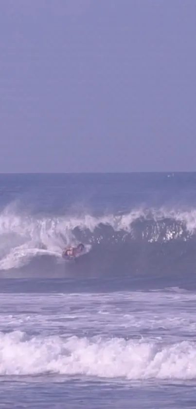 Surfer riding a large wave on a pale lavender ocean.