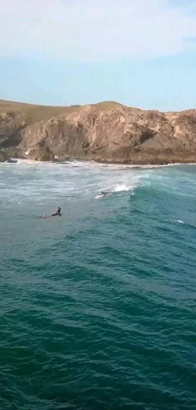 Surfers on teal ocean waves with rocky cliffs in the background.