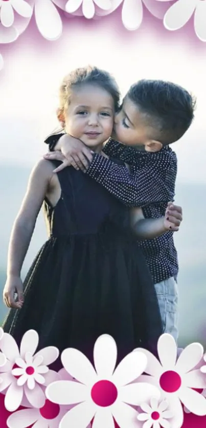Two children embracing with floral pink border wallpaper.
