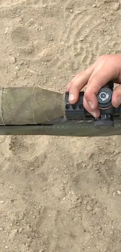 Close-up of someone adjusting a sniper scope in a sandy environment.