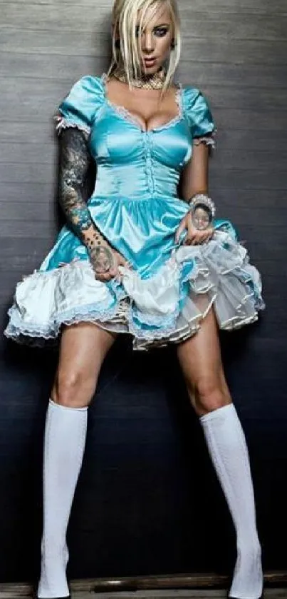 Tattooed woman in blue dress standing confidently with a dark background.