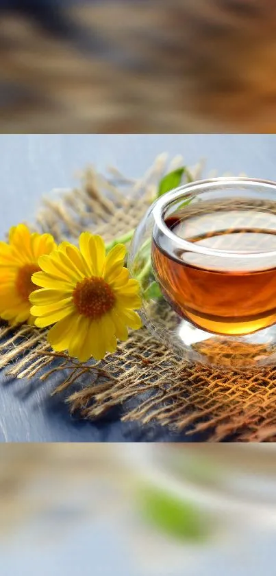 Glass cup of tea with yellow flowers on a rustic mat.