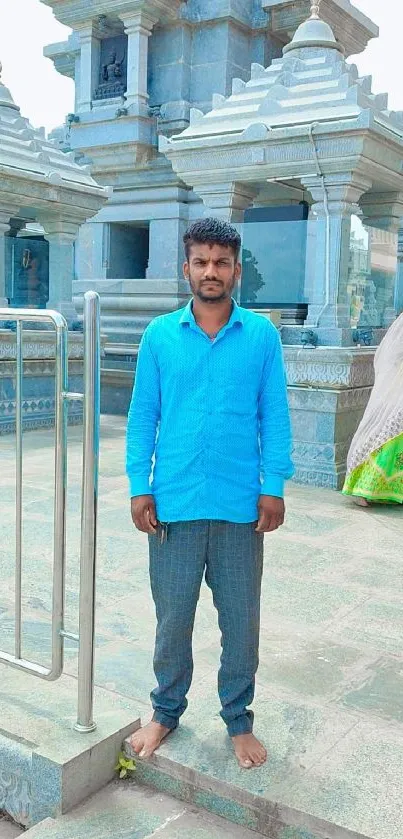 Man in blue shirt standing in front of a temple.