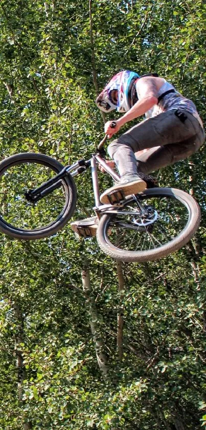 BMX rider performs a mid-air stunt against a green tree backdrop.