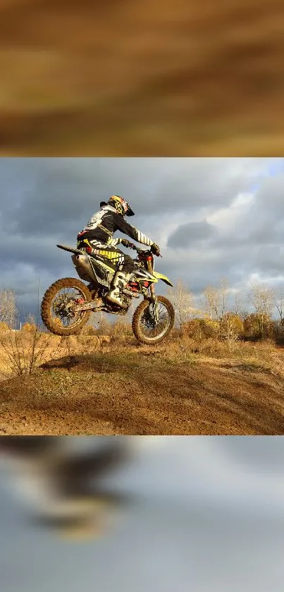 Motocross rider jumps on dirt bike against a cloudy sky.