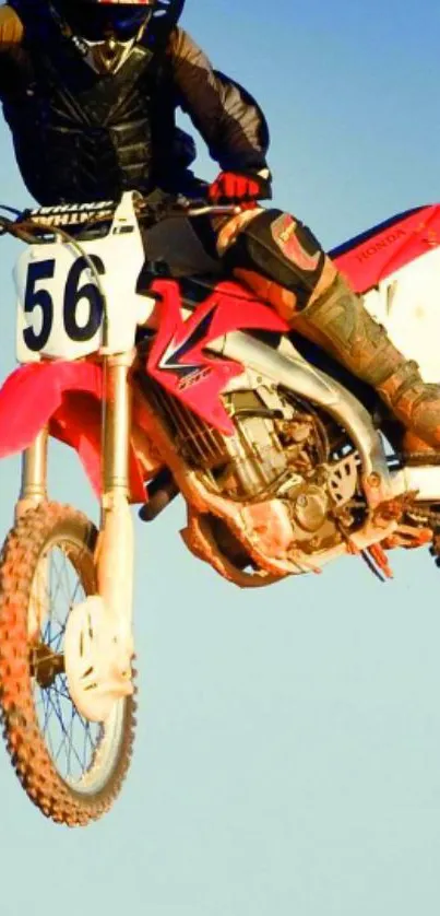 Dirt biker performs a high-flying jump against a blue sky backdrop.