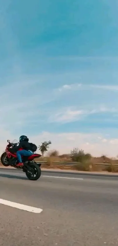 Motorcyclist performing a wheelie on a country road under a blue sky.