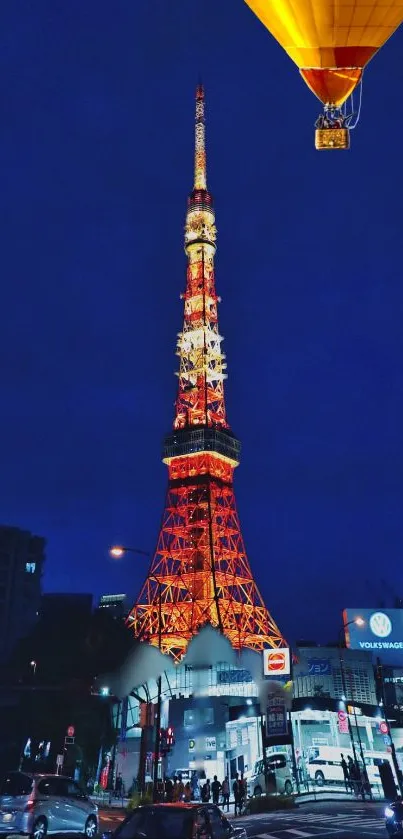 Tokyo Tower illuminated at night against a dark blue sky with a floating hot air balloon.