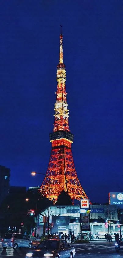 Tokyo Tower illuminated at night with cars passing by and deep blue sky backdrop.