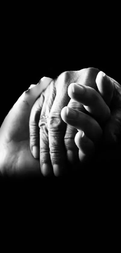 Black and white photo of two hands holding on a black background.