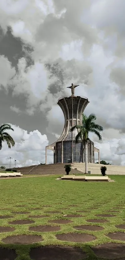 Tower under a cloudy sky with palm trees and green landscape.