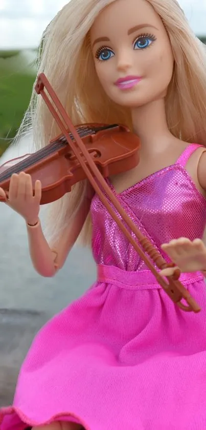 Blonde doll in pink dress playing a violin outdoors.