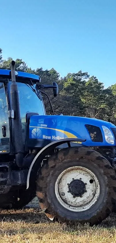 Blue tractor in a field under a clear sky with trees in the background.