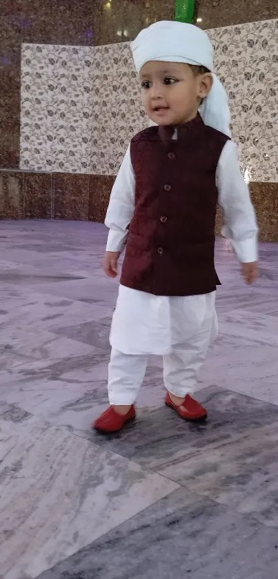 Young child in traditional attire with a maroon vest and white turban.