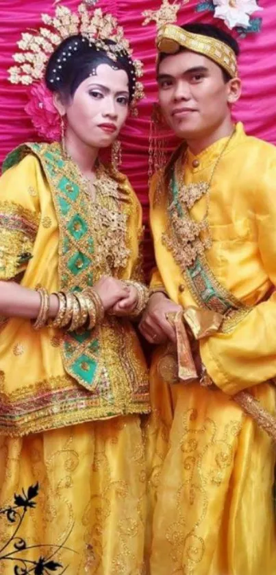 Couple in vibrant traditional yellow attire with pink backdrop.