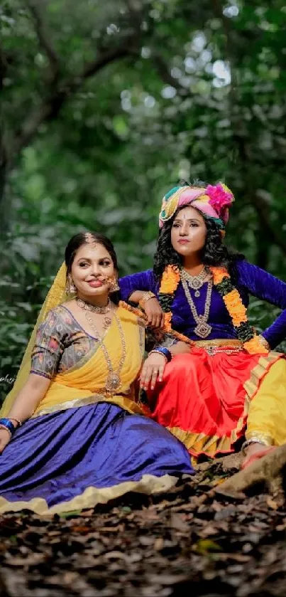 Two women in traditional attire sitting in a lush green forest.