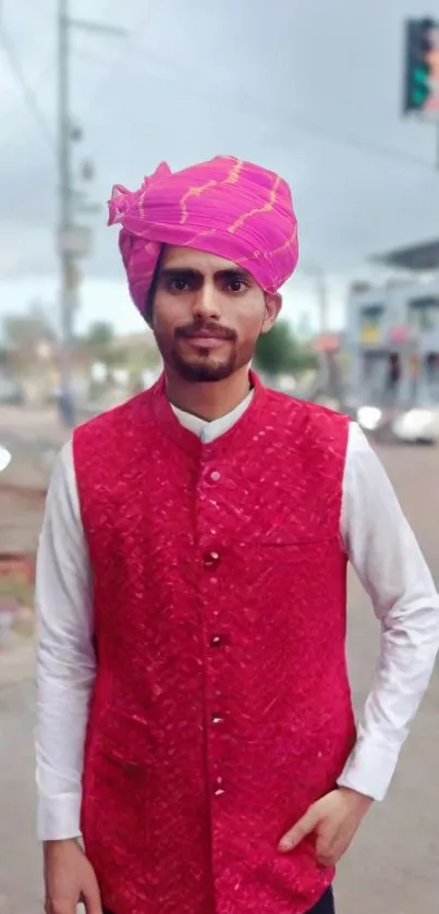 Man in a pink traditional vest and turban outdoors.