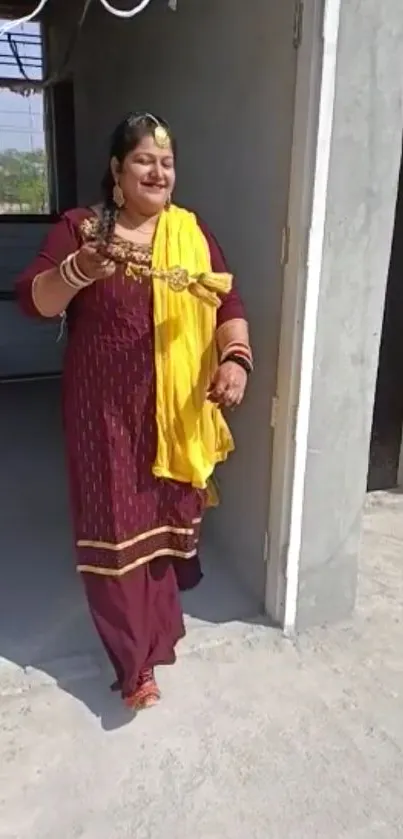 Woman in maroon dress with yellow scarf standing in doorway.