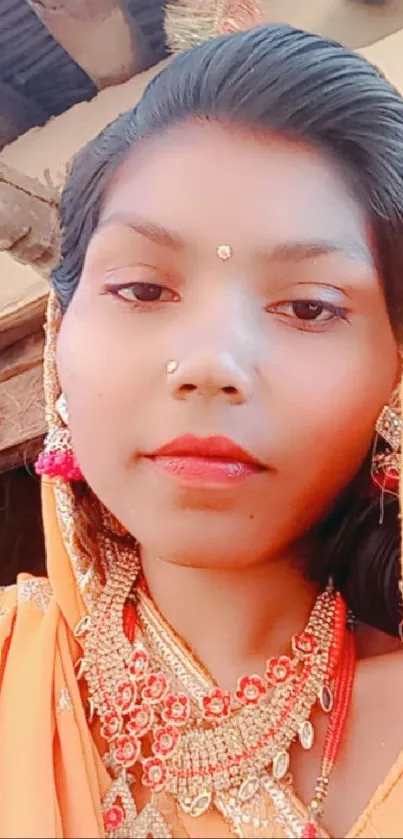 Woman in traditional Indian attire with vibrant jewelry and orange hues.