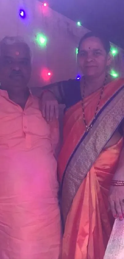 Couple in traditional Indian attire with colorful lights.