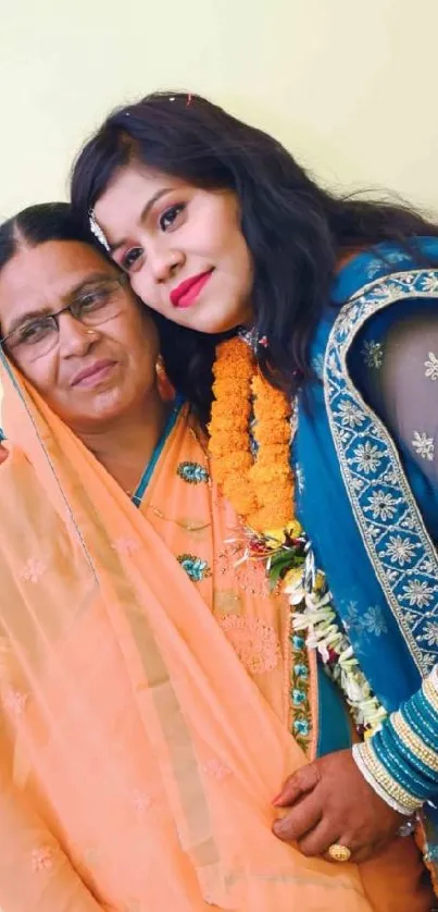 Two women in vibrant traditional Indian attire, smiling and embracing.