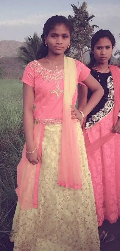 Two girls in vibrant traditional attire in a rural field setting.