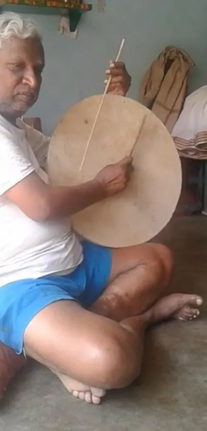 Elderly man playing a traditional drum in a rustic setting.